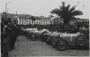 Fotografía de los automóviles participantes en el V Gran Premio de San Sebastián aparcados en la plaza Oquendo de Donostia-San Sebastián. En primer término, el automóvil Bugatti del piloto Emilio Materassi. Con el nº 20, el automóvil Amilcar del piloto Martín. Con el nº 23 el Bugatti del piloto André Dubonnet. Ycon el nº 10, un Hudson del piloto Bernhardt. Al fondo de la imagen, el desaparecido frontón Urumea