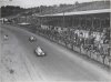 Fotografía de dos automóviles compitiendo el Gran Premio de España de 1934 bajo la antenta mirada del público de las tribunas y de la ladera